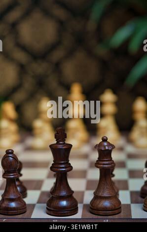 Nahaufnahme hölzerner Schachfiguren auf einem Schachbrett mit Fokus auf den schwarzen König und die Königin mit verschwommenen weißen Stücken im Hintergrund Stockfoto