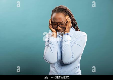 Das frustrierte weibliche Modell zeigt Anzeichen von Migräne und Müdigkeit, überfordert von Unwohlsein. Kranke afroamerikanische Frau, die ihre Schläfe berührt, drückt Spannung und Frustration durch anhaltende Kopfschmerzen aus. Stockfoto