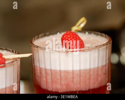 Nahaufnahme eines eleganten Himbeerdesserts, serviert in einem Glas, mit cremigem weißem Mousse und roten Fruchtschichten, gekrönt mit einer frischen Himbeere. Stockfoto