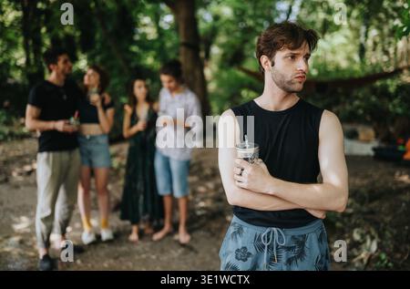 Gruppe von Freunden in einem Park mit einem Mann davor, der einen Drink hält, zwangloses Treffen im Freien Stockfoto