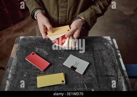 Junger Erwachsener, der Farbmuster vergleicht, während er auf der Werkstattbank steht Stockfoto