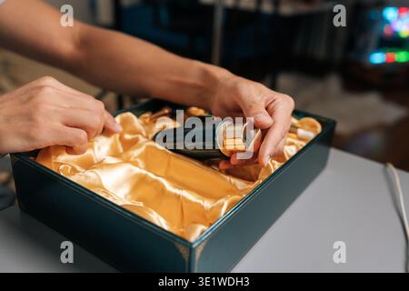 Nahaufnahme der Hände eines nicht erkennbaren Mannes, der die Flasche aus einer dunkelgrünen Geschenkbox öffnet und eine elegante Kollektion von Pflegeprodukten für Männer enthüllt Stockfoto