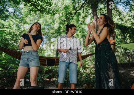 Drei Freunde tanzen und lachen in einem üppigen Park mit Hängematten Stockfoto