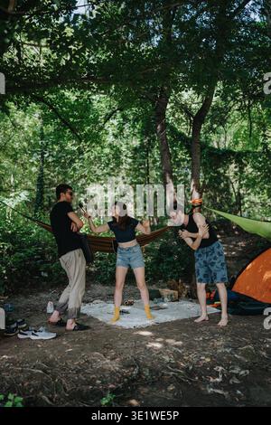 Freunde, die im Wald campen; eine Frau interviewt einen Mann, während andere lachen und entspannen Stockfoto