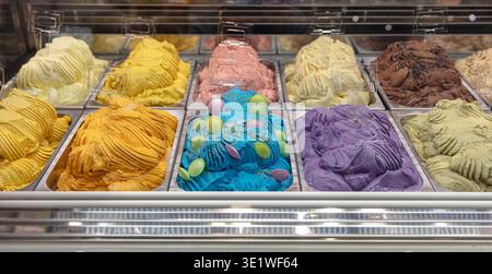 Eine Vielzahl von bunten Eissorten werden in Metalltabletts in einem gekühlten Schaufenster gezeigt, Menüs Restaurants Cafés und andere kommerzielle Speisen Stockfoto