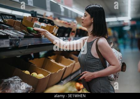 Frau, die reife Avocado auswählt, während sie in einem Supermarkt einkaufen Stockfoto