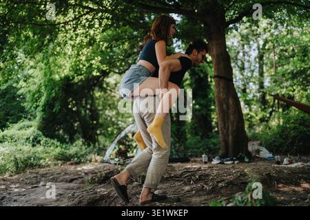 Verspielter Huckepack-Moment, während ein Paar einen Campingtag im Wald genießt Stockfoto