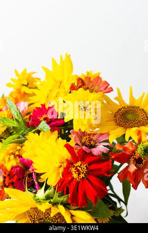 Ein Blumenstrauß mit Sonnenblumen und Zinnien sitzt in einer Vase vor einem schlichten Hintergrund. Die Blumen sind lebendig und bunt und zeigen eine Mischung aus Gelb, o Stockfoto