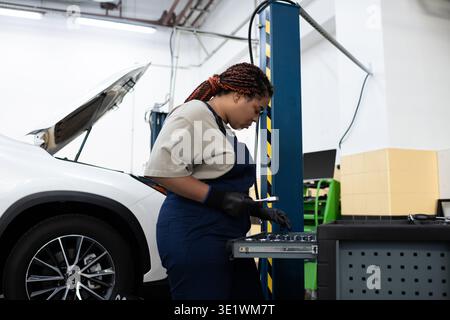 Fokussierte Mechanikerin in Overalls repariert ein Fahrzeug in einer belebten Garage. Stockfoto