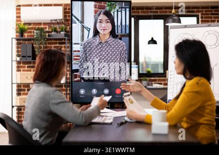 Unternehmensberater führen eine virtuelle Diskussion, bei der sie mit einem Remote-Kunden über den Kostenbericht des Unternehmens diskutieren. Asiatische Frauen analysieren Projektdaten während eines Online-Video-Meetings und prüfen wichtige Updates. Stockfoto
