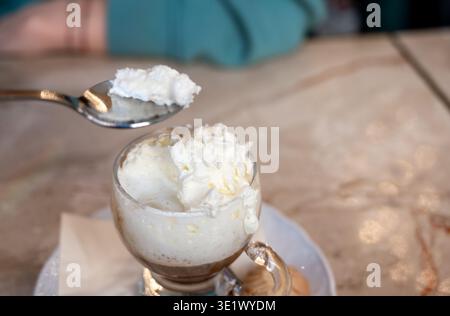Mailand, italien, 1. april 2024. Person, die ein Kaffeegetränk mit süßer Schlagsahne genießt, mit einem Löffel als Dessert, während sie in einem Café frühstückt Stockfoto