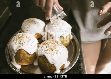 Créteil, Frankreich - 27. April 2019: Nahaufnahme einer Person, die traditionelle Osterkuchen mit weißer Glasur und bunten Streuseln in einer Küche dekoriert. Stockfoto