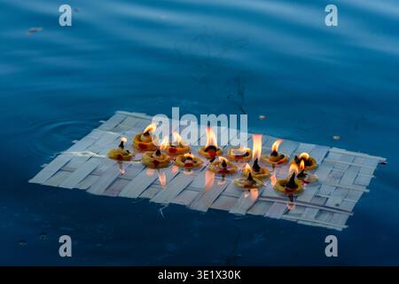 Ein kleines Holzfloß mit mehreren brennenden Öllampen schwimmt auf dem blauen Wasser des Pichola-Sees in Udaipur und hinterlässt eine leichte Rauchspur. Udaipur Stockfoto