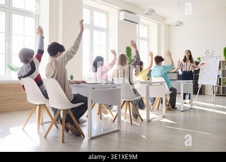 Die Schüler der High School heben die Hände in einem hellen Klassenzimmer, während der Lehrer den Unterricht leitet Stockfoto