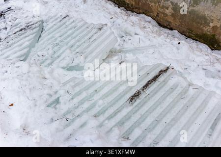 Schwere Welleisplatten auf Neuschnee verstreut, eine deutliche Erinnerung an die Gefahr im Winter. Potenziell gefährliche gefrorene Stücke aus dem Dachabstand Stockfoto