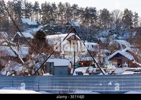 Malerisches Winterdorf mit rustikalen, schneebedeckten Landhäusern, eingebettet zwischen satinierten Bäumen. Eine ruhige, schneebedeckte Landschaft unter strahlendem Sonnenlicht Stockfoto