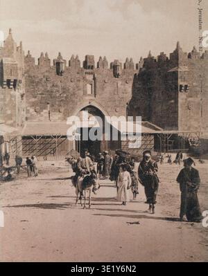 Das Damaskus-Tor ist ein nördlicher Haupteingang zur Altstadt von Jerusalem, der in die osmanischen Stadtmauern integriert wurde, die 1537 unter Sultan Suleiman dem Prachtvollen wiederaufgebaut wurden. Das Tor verbindet die historische Route in Richtung Nablus und historisch weiter nach Damaskus, wodurch das Gebäude seinen englischen Namen erhält. Der Archivfotograf erscheint als Postkartenbild, das in der Postkartensammlung der israelischen Nationalbibliothek aufbewahrt wird und das Tor und die umliegende Marktaktivität im frühen 20. Jahrhundert dokumentiert. Stockfoto