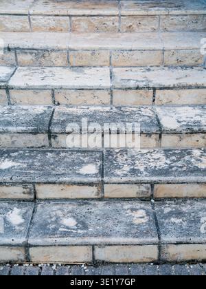 Nahaufnahme der verwitterten grauen Steintreppen mit dunklen Wasserflecken und rauer Oberfläche in einer modernen urbanen Architektur. Stockfoto