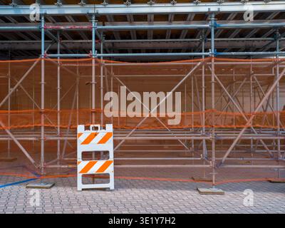 Baustelle mit Gerüstrahmen aus Metall und orangefarbenem Sicherheitsnetz über einem gemauerten Bürgersteig in einer Stadtstraße. Stockfoto
