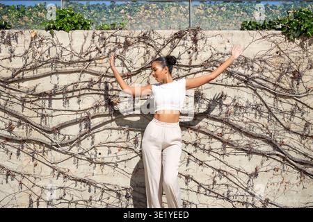 Frau, die Freiheit ausdrückt durch energischen Sprung gegen üppige Weinweinwand im Sonnenlicht Stockfoto