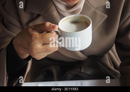 Frau, die eine Kaffeetasse in einer gemütlichen Umgebung hält Stockfoto