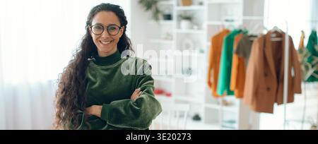Frau steht selbstbewusst in einem Studio mit farbenfroher Kleidung im Hintergrund Stockfoto
