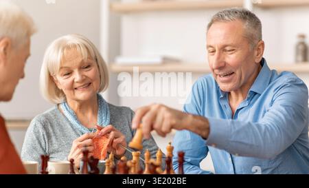 Ältere Menschen genießen Schach und Stricken in gemütlicher Innenumgebung am Nachmittag Stockfoto