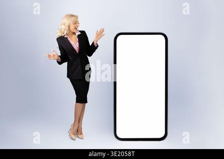 Junge Frau in Geschäftskleidung präsentiert einen großen leeren Bildschirm im Studio-Setting Stockfoto