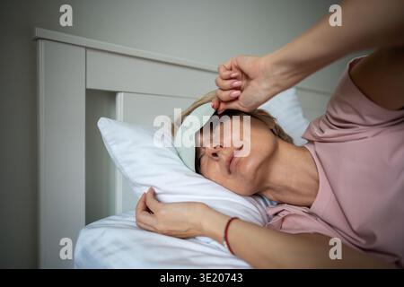 Verschlafene, entspannte Frau, die am frühen Morgen aufwacht und aus der im Bett liegenden Augenmaske blickt. Stockfoto