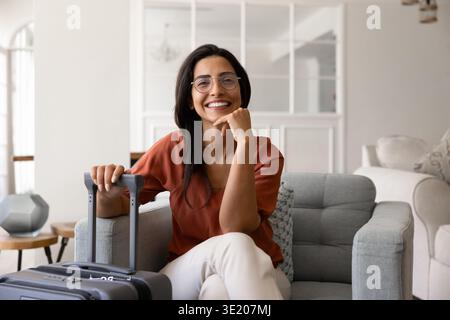 Porträt einer brasilianischen Touristin, die im Sessel mit Koffer sitzt Stockfoto