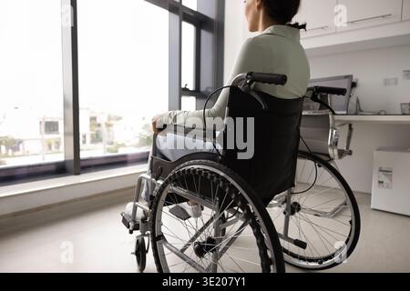 Rückansicht einer Patientin im Rollstuhl, die allein drinnen sitzt Stockfoto