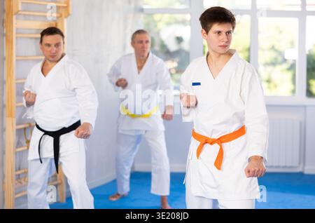 Kampfhaltung von Männern unterschiedlichen Alters während des Gruppenkaratetrainings. Guy trainiert Schläger Stockfoto