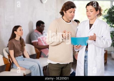 Europäischer Mann, der nach einem Interview am Empfang steht und mit einer Krankenschwester plaudert Stockfoto