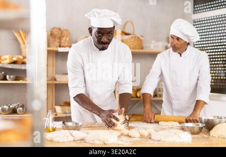 Zwei Bäcker kneten Teig und Rollen ihn aus Stockfoto