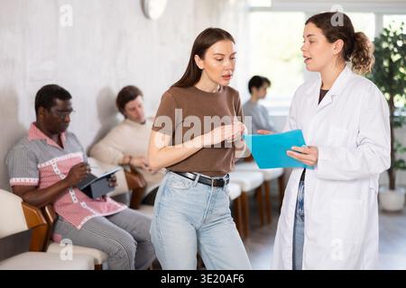 Junge Krankenschwester oder Ärztin, die mit der Frau im Empfangsbereich spricht Stockfoto