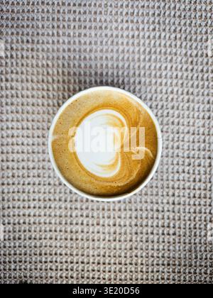 Eine weiße Tasse frisch zubereiteten Kaffee mit Milch auf dem grauen Tischtuch mit einer grauen strukturierten Tischdecke im Hintergrund. Minimalistisches Konzept, Thai Stockfoto