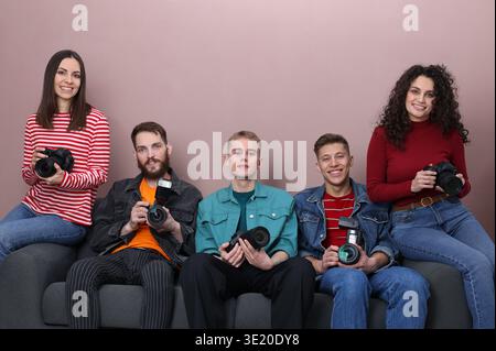 Gruppe von Fotografen mit professionellen Kameras auf Sofa vor farbigem Hintergrund Stockfoto