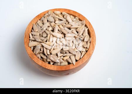 Eine hölzerne Schüssel gefüllt mit Muscheln Sonnenblumensamen auf weißem Hintergrund Stockfoto