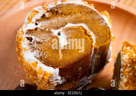 Nahaufnahme eines Kürbis-Rollkuchen mit Creme Frosting und zerstoßenen Nüssen auf einer Holzplatte Stockfoto