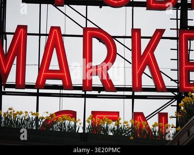 Nahaufnahme des beleuchteten Pike Place Market-Schilds im Zentrum von Seattle, Washington, USA, mit Frühlingsblumen im Vordergrund Stockfoto