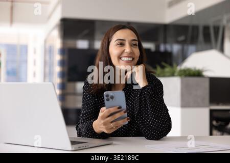 Fröhliche, glückliche Angestellte aus dem Nahen Osten, die ihr Handy benutzt Stockfoto