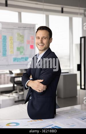 Porträt fröhlicher, zuversichtlicher Geschäftsmann im mittleren Erwachsenenalter, der auf dem Schreibtisch sitzt Stockfoto
