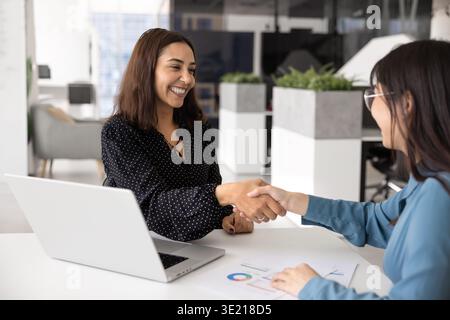 Fröhliche junge Geschäftsfrau aus dem Nahen Osten, die sich mit einem asiatischen Berater die Hand schüttelt Stockfoto
