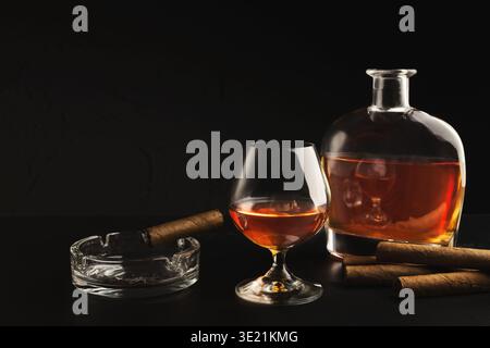 Glas mit Cognac, Flasche und Zigarre auf schwarzem Hintergrund Stockfoto