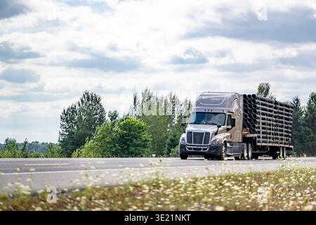 Beige Sattelzugmaschine in Industriequalität mit verlängerter Fahrerkabine für den Transport befestigter Kunststoffrohre auf dem Trittbrett Semi tr Stockfoto