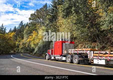 Big Rig Red Sattelzugmaschine mit verlängerter Kabine für LKW-Fahrer Ruhe Transport befestigter Holzfracht auf Treppendeck Auflieger, der auf dem Sieg läuft Stockfoto