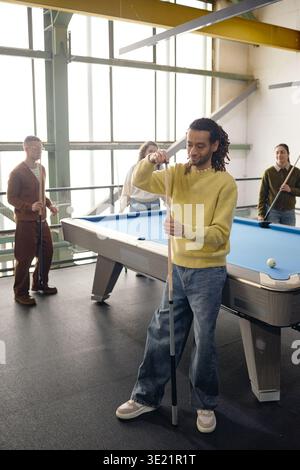 Vertikal des jungen birassischen Mannes, der Pool Cue kreidet, während er Spiel mit Freunden spielt Stockfoto