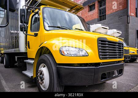 Gelbe Sattelzugmaschine für industrielle Anwendungen mit mittelbelastetem Lkw und Kühlkoffer, die in Reihe mit einem anderen Auflieger auf Industrieparke steht Stockfoto