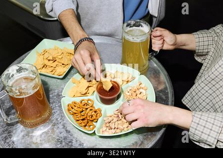 Junge Erwachsene Mann und Frau teilen Bier und Snacks bei einem Social Meeting Stockfoto