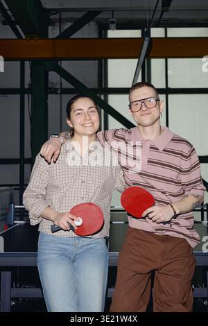 Vertikales Porträt eines jungen Mannes und einer lächelnden Frau, die Tischtennis-Paddles halten Stockfoto